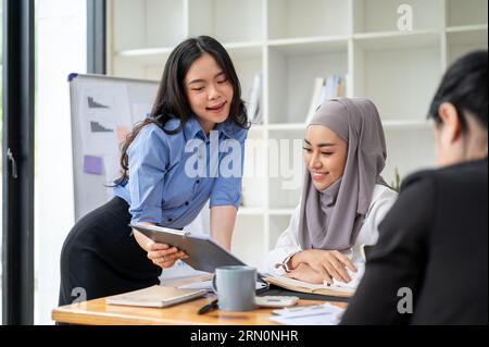 A beautiful young Asian businesswoman is discussing ideas and brainstorming a new project with her diverse colleagues during the meeting. Muslim and A Stock Photo