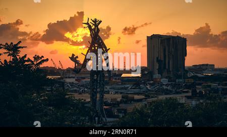 The Gesture, sculpture to honor victims of port explosion at Port of Beirut in rays of setting sun and damaged grain elevator at background. Beirut, L Banque D'Images