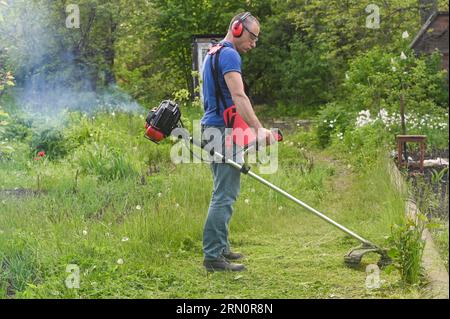 L'homme tond l'herbe avec un scythe d'essence. Banque D'Images