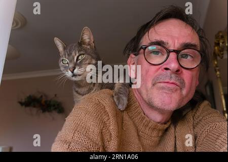 Un homme portant des lunettes avec un adorable chat tabby perché sur son épaule Banque D'Images