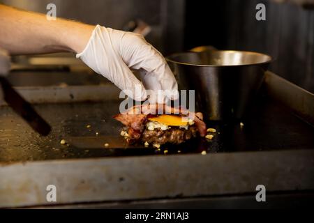 Chef cuisinant des hamburgers, friture de viande de bœuf sur la poêle dans la cuisine du restaurant. Ouvrier de restauration rapide préparant des côtelettes de porc Banque D'Images