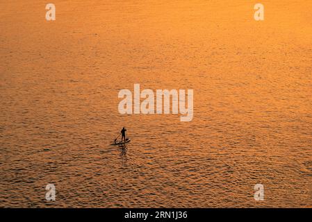 Les gens aventureux sur une planche de stand up paddle pagaie pendant un lever de soleil lumineux et vibrant Banque D'Images