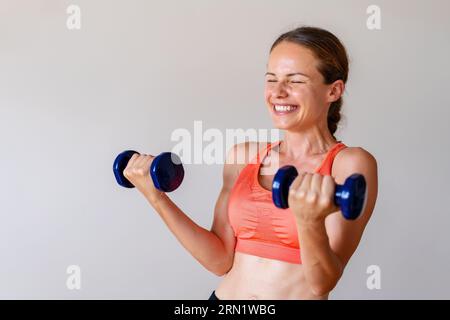 Jeune athlète féminine s'amuse tout en faisant des exercices de gym avec des haltères. Banque D'Images