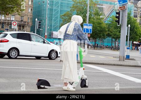 Femme avec un foulard blanc debout sur un scooter électrique au carrefour du centre-ville. Banque D'Images