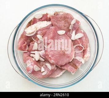 Porc cru tranché saupoudré de poivre et d'oignon haché dans un bol en verre. Vue de dessus, gros plan. Banque D'Images