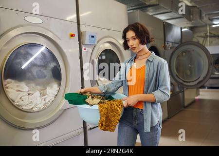 jeune femme asiatique tenant le panier avec des vêtements près des machines à laver dans la blanchisserie publique Banque D'Images