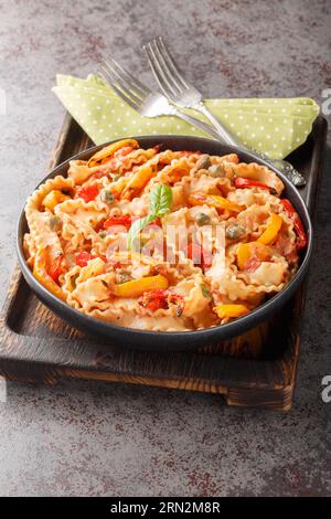 Mafalda Pasta en sauce tomate crémeuse avec câpres et gros plan de papper cuit sur l'assiette sur la table. Vertical Banque D'Images