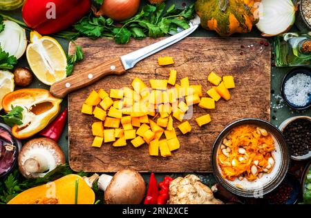 Fond alimentaire. Couteau de citrouille pelée crue en dés et légumes sur une planche à découper en bois rustique. Légumes, champignons, racines, épices - ingrédients pour v Banque D'Images