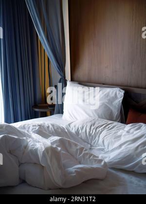 Draps blancs froissés linge de lit avec oreiller et couverture dans les lumières douces du matin, ambiance confortable de repos et de détente chambre, hôtel de lit vide non fait Banque D'Images