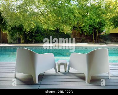 Chaises en plastique blanc design moderne au côté de la piscine et jardin extérieur, véranda confortable décorée, terrasse en bois, espace d'intimité de cour arrière pour r Banque D'Images