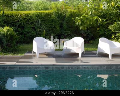 Chaises en plastique blanc design moderne au côté de la piscine et jardin extérieur, véranda confortable décorée, terrasse en bois, espace d'intimité de cour arrière pour r Banque D'Images