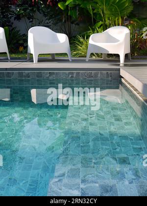 Chaises en plastique blanc design moderne au côté de la piscine et jardin extérieur, véranda confortable décorée, terrasse en bois, espace d'intimité de cour arrière pour r Banque D'Images