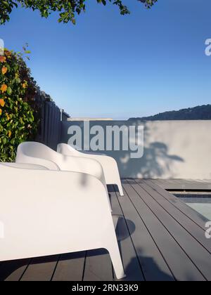 Chaises en plastique blanc design moderne au côté de la piscine et jardin extérieur, véranda confortable décorée, terrasse en bois, espace d'intimité de cour arrière pour r Banque D'Images