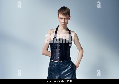 personne queer en corset noir et short posant sur fond gris, modèle androgyne, confiant Banque D'Images