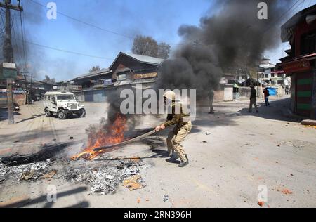 (150410) -- SRINAGAR, 10 avril 2015 -- un policier indien enlève un pneu en feu dans une rue lors d'affrontements avec des manifestants cachemiris à Srinagar, capitale estivale du Cachemire contrôlé par l'Inde, le 10 avril 2015. Vendredi, la police indienne a tiré des dizaines d'obus lacrymogènes et a eu recours à la matraque pour chasser les manifestants protestant contre le plan du gouvernement indien de construire des colonies séparées pour les hindous cachemiris, ont déclaré des témoins. CACHEMIRE-SRINAGAR-AFFRONTEMENTS JavedxDar PUBLICATIONxNOTxINxCHN Srinagar avril 10 2015 à la police indienne enlève un pneu en feu d'une rue lors des affrontements avec les manifestants cachemiris i Banque D'Images