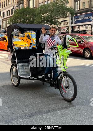 Le chauffeur de Pedicab donne une vague amicale alors qu'il passe sur la 5th Avenue dans le centre-ville de Manhattan. Banque D'Images