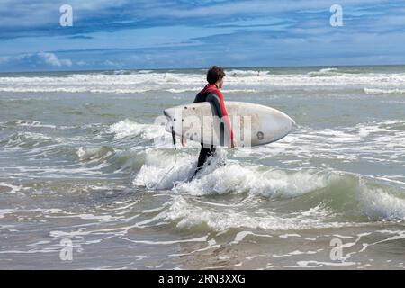 Surfeur portant planche de surf et se mettre dans l'eau à Wembury Beach , Cornwall, Royaume-Uni Banque D'Images