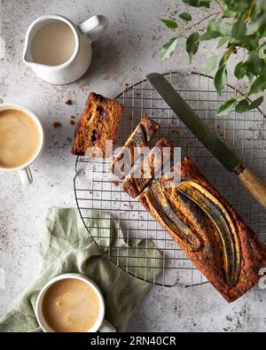 Pain à la banane tranché sur un fond texturé blanc. Il y a quelques tranches sur la table et quelques tasses de café. Image de style de vie léger d'un ensemble familial Banque D'Images