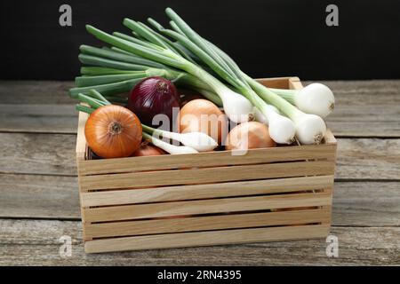 Crate with different kinds of onions on wooden table Stock Photo