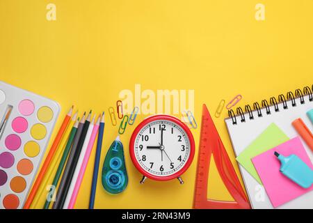 Composition de pose plate avec différentes papeterie scolaire et réveil sur fond jaune, espace pour le texte. Retour à l'école Banque D'Images