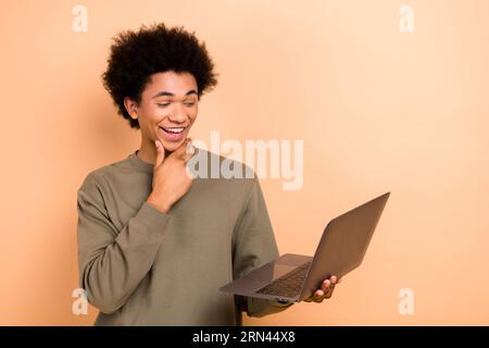 Portrait of excited handsome person hand touch chin use wireless netbook watch video isolated on beige color background Banque D'Images