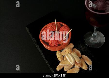 Chorizo ibérique, saucisse ibérique, frit dans un pot d'argile avec du pain et du vin rouge tapa typiquement espagnol isolé sur fond noir et espace copie Banque D'Images