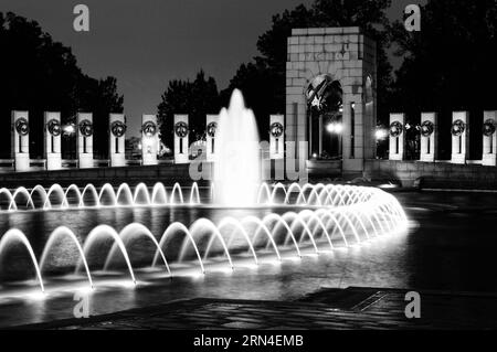 Fontaine commémorative de la seconde Guerre mondiale la nuit, Washington, D.C. photographie en noir et blanc montrant les jets d'eau illuminés et l'architecture environnante. Banque D'Images