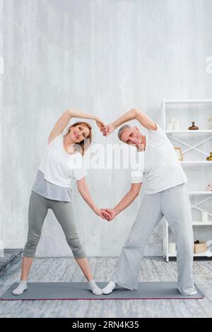 Joyeux couple senior faisant la forme du cœur avec leurs mains tout en exerçant à la maison Banque D'Images