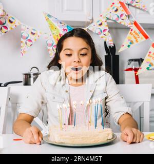 Fille d'anniversaire surprise soufflant un gâteau avec des bougies allumées Banque D'Images