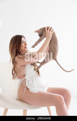 Belle jeune femme enceinte regardant le chat dans une chaise blanche Banque D'Images