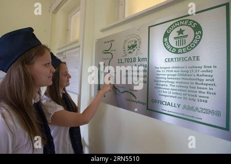 (150613) -- BUDAPEST, 13 juin 2015 -- des filles regardent la plaque du record du monde Guinness à la gare Huvosvolgy du chemin de fer pour enfants à Budapest, Hongrie, le 13 juin 2015. Le chemin de fer à voie étroite de 11,7018 km relie les gares de Huvosvolgy et Szechenyihegy à Budapest. Il est en service continu depuis l'inauguration des 3,2 premiers kilomètres de voie le 31 juillet 1948. Les moteurs sont entraînés par des ingénieurs adultes, et les enfants âgés de 10 à 14 ans en service sont continuellement supervisés par des employés des chemins de fer adultes. En dehors de cela, les enfants font leur travail seuls. Le Children s Railway a reçu le Banque D'Images