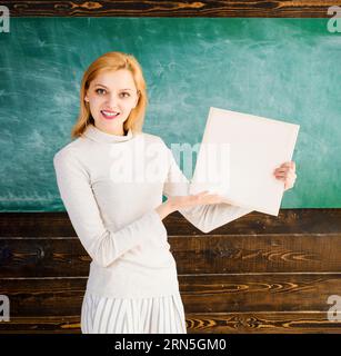 Retour à l'école. Travail des enseignants. Enseignant souriant avec dossier dans la salle de classe. Étudiante universitaire avec cahier près du tableau. Journée du savoir Banque D'Images