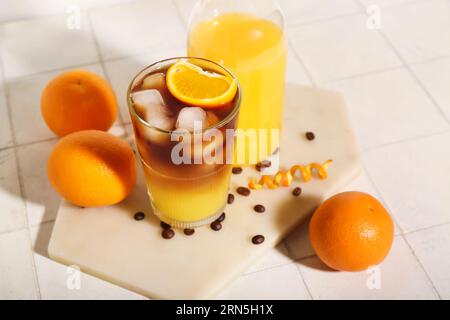 Verre d'espresso orange savoureux et bouteille avec du jus sur fond de tuile blanche Banque D'Images