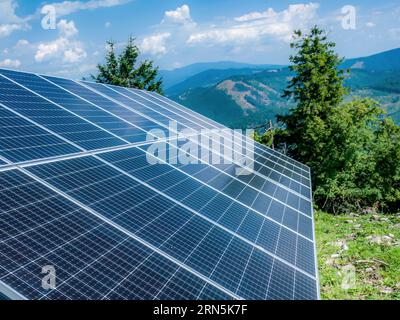 Gros plan de la station de panneaux solaires montée sur une pente de montagne, avec un beau panorama des montagnes Beskid Zywiecki en arrière-plan, Pologne Banque D'Images