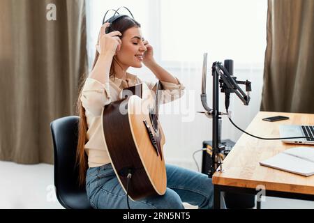 Vue latérale musicien féminin mettant des écouteurs enregistrer la chanson jouer guitare acoustique Banque D'Images