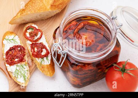 Tomates séchées au soleil à l'huile d'olive dans un bocal en verre et sandwichs prêts à l'emploi sur la table Banque D'Images