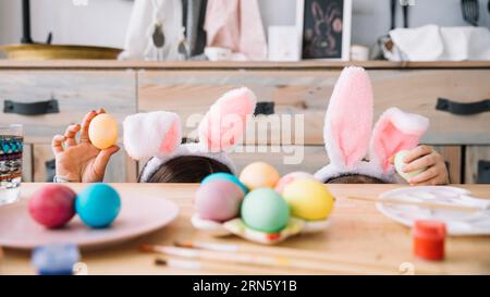 Mère avec enfant oreilles de lapin cachant la table avec des oeufs de couleur Banque D'Images