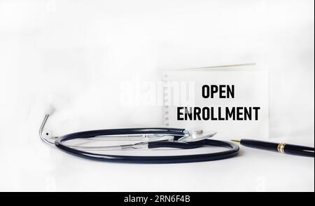 Stethoscope and notepad with text OPEN ENROLLMENT on white background. Medical concept. Stock Photo