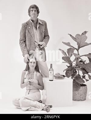 1970S COUPLE À LA MODE HOMME DEBOUT FEMME ASSISE TABLE CUBE AVEC BOUTEILLE DE VIN TENANT LES DEUX VERRES DE VIN REGARDANT LA CAMÉRA - F13393 HAR001 HARS CONTACT OCULAIRE CUBE STYLES DE BOISSON JUMPSUIT COIFFURE FLUIDE RAISINS MAISON PLANTE LIQUEUR ALCOOL ALCOOL SPIRITUEUX ALCOOL ALCOOL BOISSONS MODES MI-ADULTE MI-ADULTE HOMME MI-ADULTE FEMME DAIM BOISSONS NOIR ET BLANC ORIGINE CAUCASIENNE HAR001 OLD FASHIONED Banque D'Images