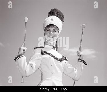 1960S SOURIANT TEEN GIRL MAJORETTE PORTANT L'UNIFORME DE BANDE ET CHAPEAU TENANT UN BATON À L'PRÊT DANS LES DEUX MAINS - P7127 HARS COPIE ESPACE DEMI-LONGUEUR PERSONNES ADOLESCENTES DIVERTISSEMENT CONFIANCE B&W CONTACT VISUEL BONHEUR JOYEUSE BATON ET EXCITATION LEADERSHIP ORGUEIL DE LOISIRS À FAIBLE ANGLE SOURIRES BANDE DE MARCHE JOYEUSE PLUME ÉLÉGANTE TEENAGED MAJOLIES JEUNES PRÉCISION TWIRL NOIR ET BLANC CAUCASIEN ETHNICITÉ HAR001 DÉMODÉ Banque D'Images