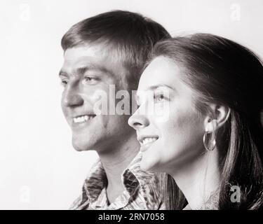 1970s PROFILE PORTRAIT OF MAN AND WOMAN BOTH SMILING WOMAN IN FOREGROUND MAN BEHIND HER - p8114 HAR001 HARS COPY SPACE FRIENDSHIP LADIES PERSONS MALES CONFIDENCE B&W PARTNER DREAMS HAPPINESS HEAD AND SHOULDERS CHEERFUL AND PRIDE SMILES CONNECTION JOYFUL STYLISH TOGETHERNESS WIVES YOUNG ADULT MAN YOUNG ADULT WOMAN BLACK AND WHITE CAUCASIAN ETHNICITY FOREGROUND HAR001 OLD FASHIONED Stock Photo