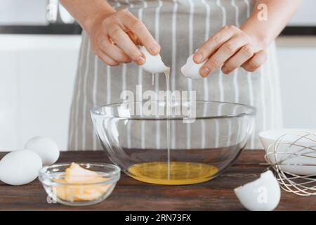 Un boulanger ou un cuisinier casse un œuf cru dans un bol. Cuisson de la pâte pour la cuisson ou le pain, faire le petit déjeuner avec des œufs, routine matinale. Bak fait maison ou fait à la main Banque D'Images