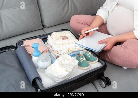 En attendant l'accouchement, la femme enceinte à la maison écrit méticuleusement sa liste de maternité, emballant sa valise avec soin, incarnant le sentiment de la future mère Banque D'Images