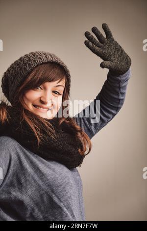 Greeting with a wool-gloved wave, a lively woman expresses her love for winter fashion. She's cozy in her gear, her brown locks and vivacious eyes shi Stock Photo