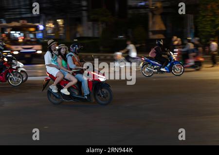 Deux filles heureuses avec des chapeaux montent à l'arrière d'un taxi moto à bangkok la nuit. Banque D'Images