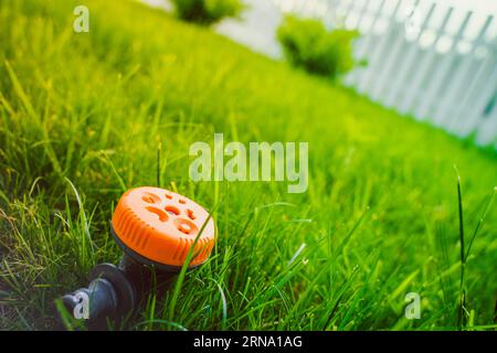 Gros plan d'un arroseur de pelouse réglable multifonctionnel. Pulvérisateur d'herbe orange avec différents modes. Arrosage secteur inséré dans le sol dans le ga Banque D'Images