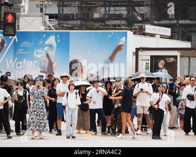 TOKYO, JAPON - 11 août 2023 : les gens qui attendent de traverser la gare de Shibuya bousculent le passage et un panneau d'affichage pour l'eau minérale Suntory. Banque D'Images