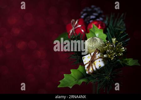 Une décoration de Noël riche, colorée et éclairée sur fond rouge étincelant avec pommes de pin, cadeaux, boules et feuilles de houx peu focalisées Banque D'Images