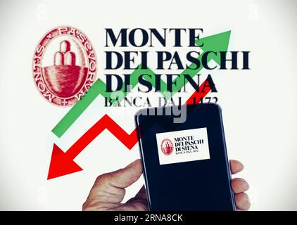 August 25th 2023 , Florence , Italy . Hand holding a cellphone with the logo of “Monte dei paschi bank “ with arrows up and down as background , conce Stock Photo