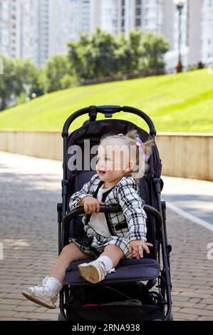 Bébé en poussette sur une promenade dans le parc d'été. Adorable petite fille assise dans une poussette. Enfant en buggy Banque D'Images